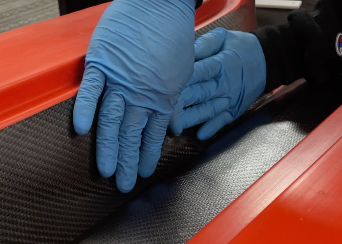 Person wearing blue gloves laying up a part with prepreg carbon fiber