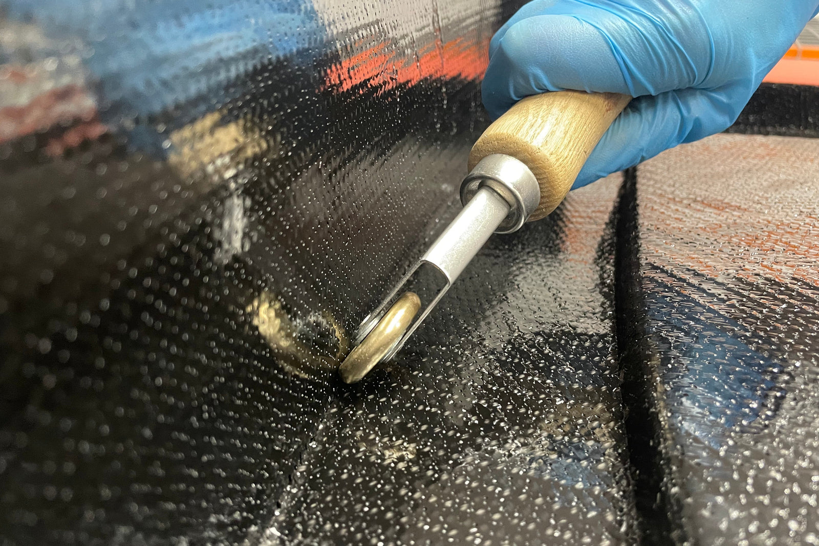 a gloved hand uses a penny roller to press prepreg into a mold